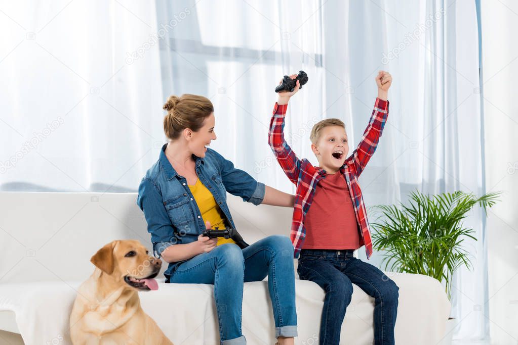 expressive mother and son playing video games while their dog sitting on floor
