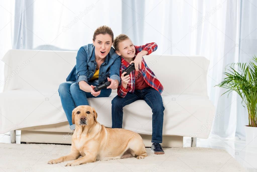 emotional mother and son playing video games while their dog lying on floor and watching