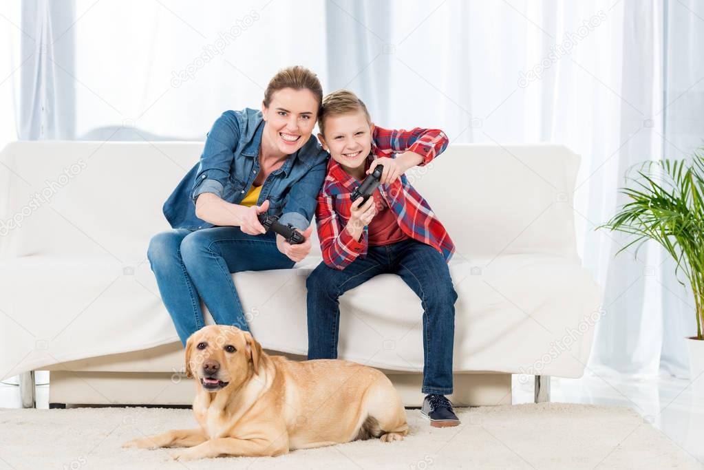 excited mother and son playing video games while their dog sitting on floor and watching