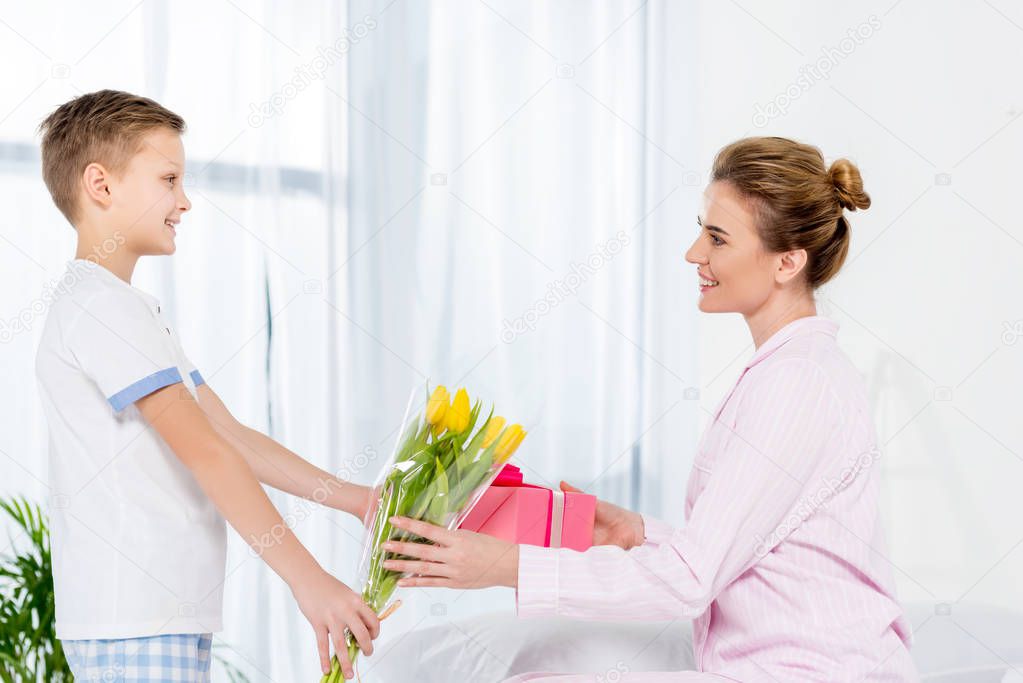 son presenting gift and tulips bouquet for mother on mothers day morning
