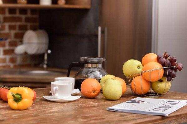 cups with coffee and vegetables with fruits on wooden table in kitchen