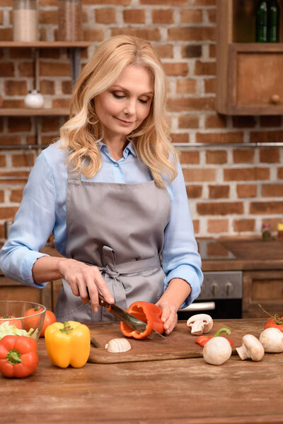 woman cutting red bell pepper on wooden board 