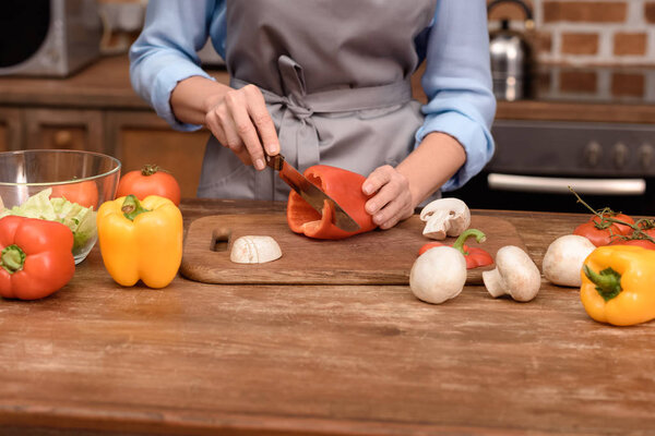 cropped image of woman cutting red bell pepper on wooden board 