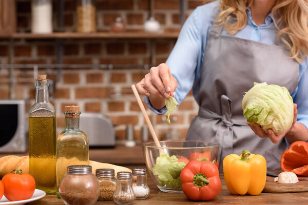cropped image of woman adding salad leaves to salad