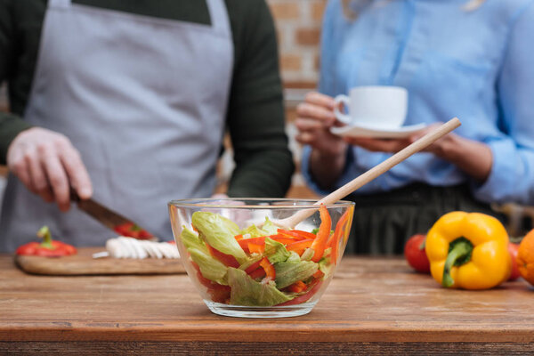 cropped image of couple preparing meal with salad on foreground