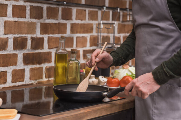 cropped image of man stirring vegetables on frying pan