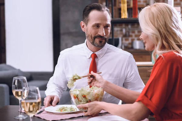 wife putting salad on husband plate during romantic dinner