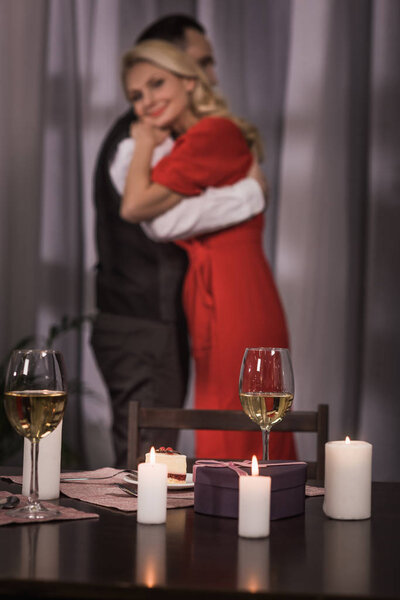 couple hugging with candles and wine in glasses on foreground