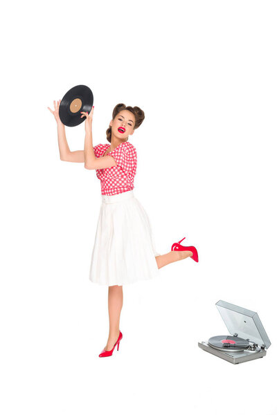 emotional woman in pin up style clothing with vinyl record in hands standing near phonograph isolated on white