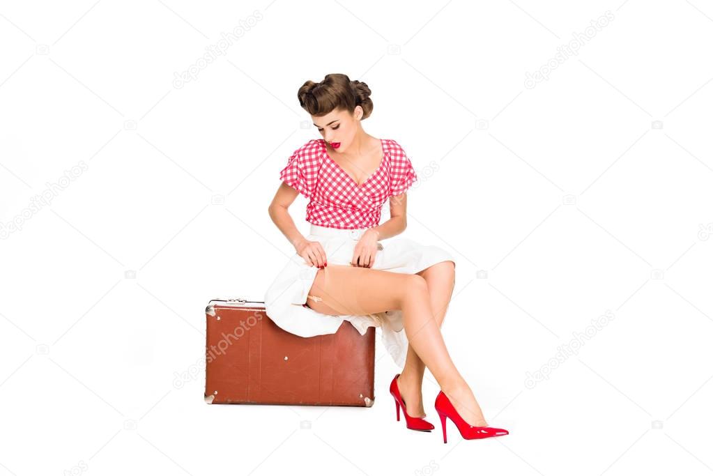 beautiful young woman in retro clothing sitting on suitcase isolated on white