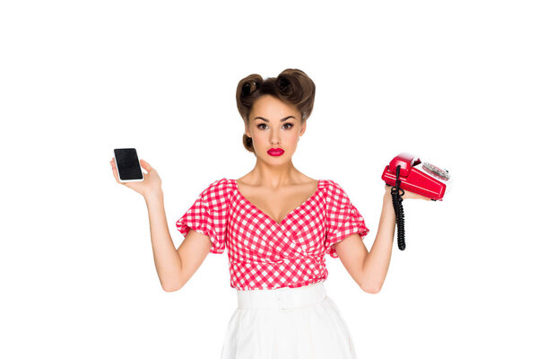 portrait of stylish woman in retro clothing holding smartphone and old telephone isolated on white
