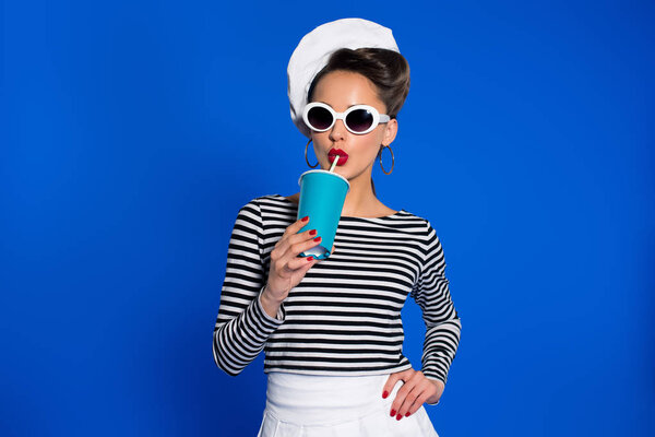 portrait of stylish young woman with beverage in paper cup isolated on blue