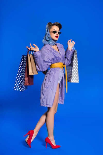 stylish woman in retro clothing with shopping bags isolated on blue