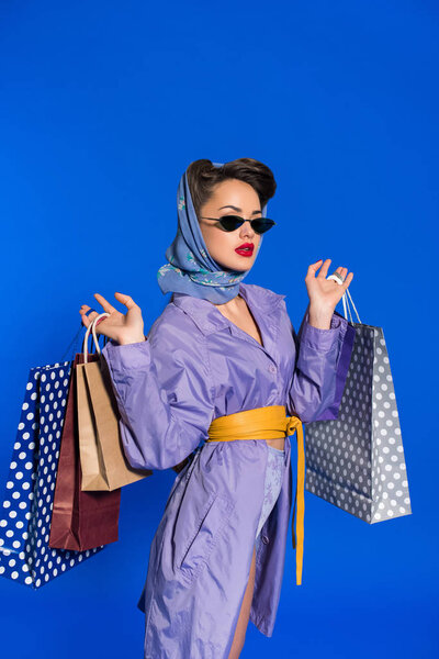 portrait of stylish woman in retro clothing with shopping bags isolated on blue