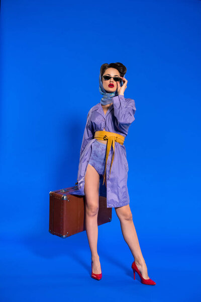 fashionable young woman in retro clothing with suitcase isolated on blue