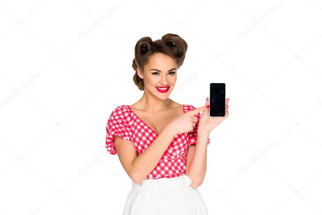 portrait of smiling pin up woman pointing at smartphone isolated on white