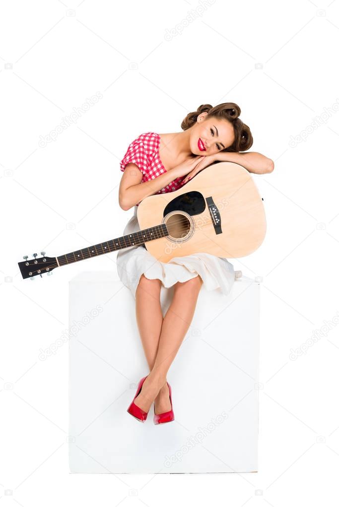smiling young woman in retro clothing with guitar sitting on cube isolated on white