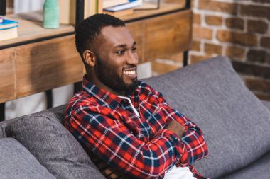 kanepe ve uzağa arıyorsunuz çapraz silah ile oturan genç Afro-Amerikan adam gülümseyen