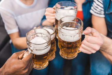 close-up partial view of young friends holding glasses of beer in hands clipart