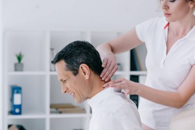 side view of masseuse doing seated neck massage for client at office clipart