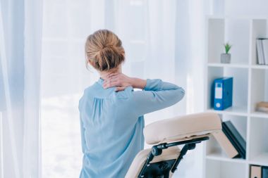 rear view of businesswoman with neckpain sitting on massage chair clipart