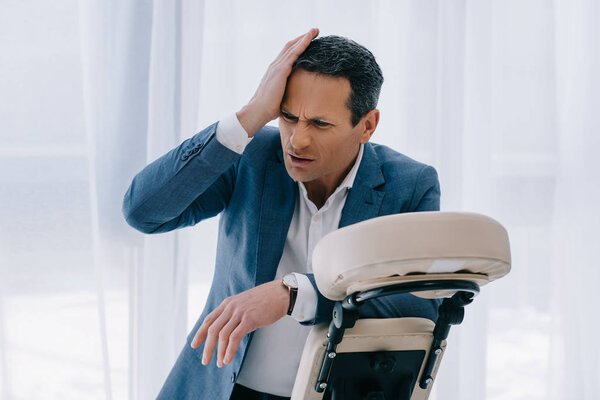 зрелый бизнесмен с головой опираясь на массажное кресло
