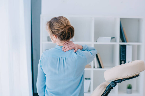 rear view of businesswoman with neckpain sitting on massage chair