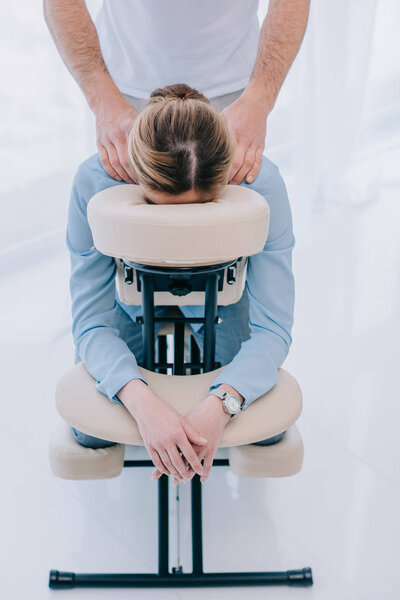 вид на массажиста, делающего офисный массаж для деловой женщины
