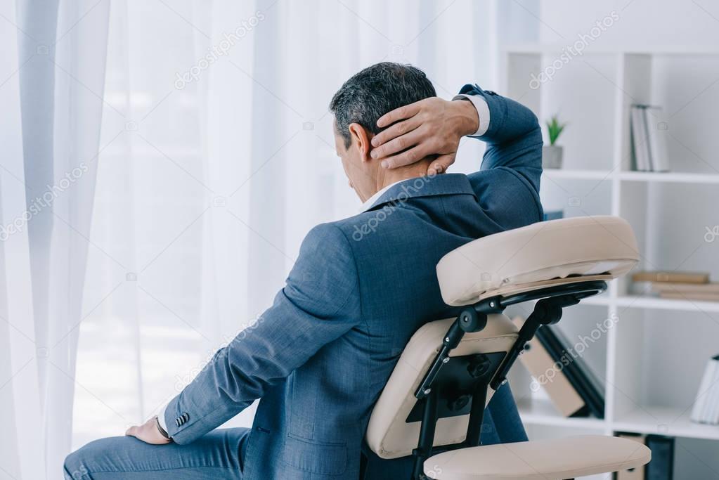 adult businessman with painful backache sitting in massage chair at office