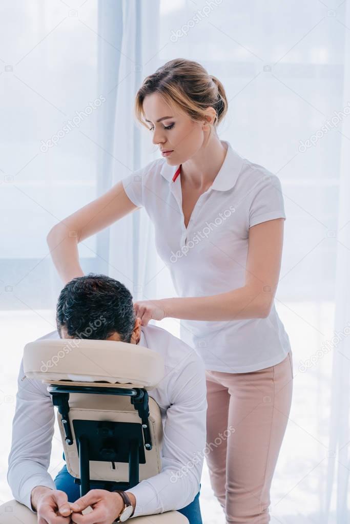 attractive masseuse doing shoulders massage on seat at office