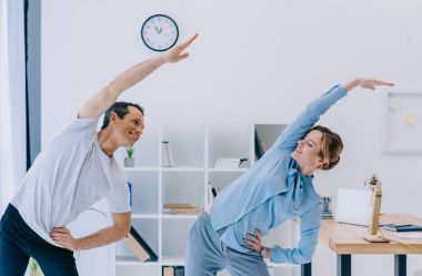 businesswoman doing side bend with trainer at office