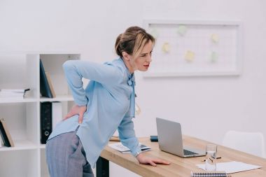 overworked adult businesswoman with backpain at office clipart