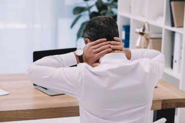 rear view of businessman with neck pain at workplace in office clipart