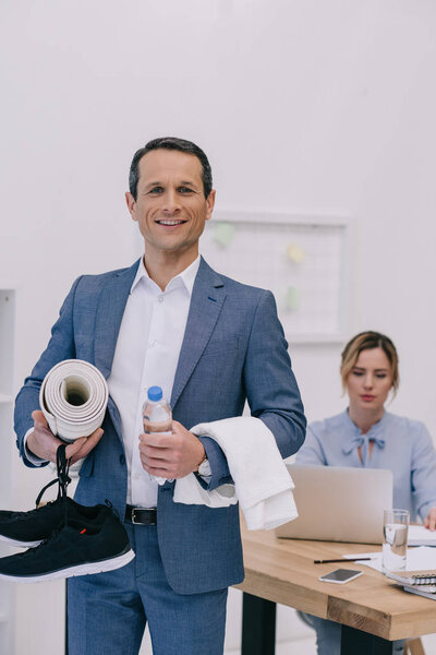 businessman with fitness equipment standing at modern office while his colleague working with computer