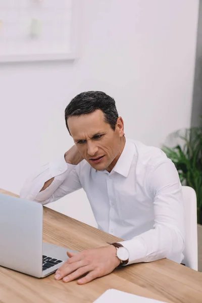 有颈部疼痛的成熟商人在办公室使用笔记本电脑 — 图库照片