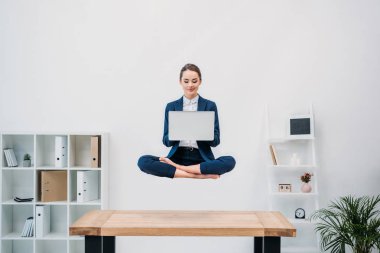 gülümseyen genç iş kadını ofiste levitating dizüstü bilgisayar kullanarak