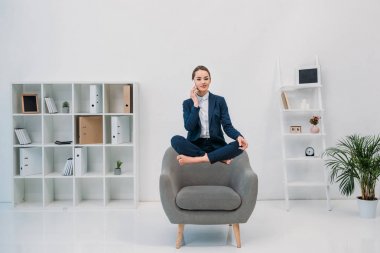 Smartphone ile konuşmak ve ofiste levitating kameraya gülümseyen genç iş kadını