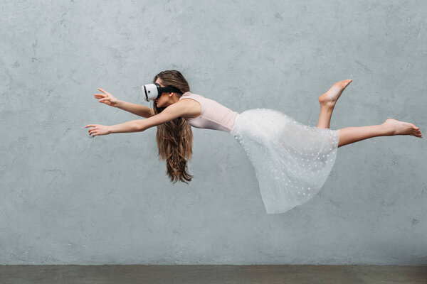 молодая босая женщина в наушниках виртуальной реальности, левитирующая на серой
 