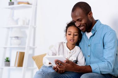 Afro-Amerikan baba ve kızı evde tablet bir şey izliyor