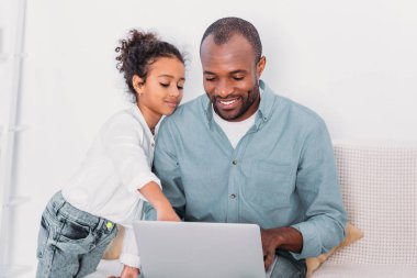 bir şey üstünde laptop gösterilen Afro-Amerikan kızı evde baba