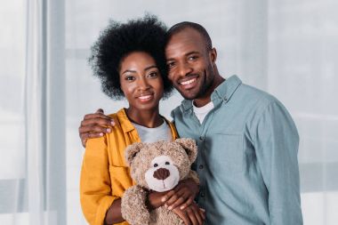 happy african american couple with teddy bear at home clipart
