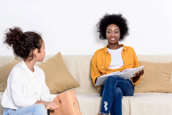 アフリカ系アメリカ人の母が読む本とロッキング ホース自宅で遊ぶ娘  — 無料ストックフォト