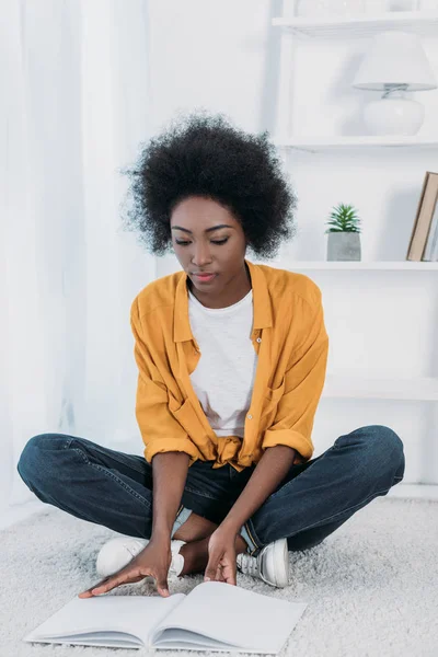 Afrikanerin Sitzt Auf Dem Boden Und Liest Buch Hause — kostenloses Stockfoto