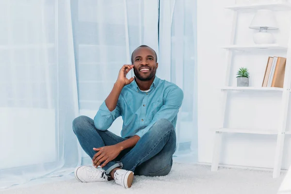 Leende Afroamerikanska Man Sitter Golvet Och Pratar Smartphone Hemma — Stockfoto