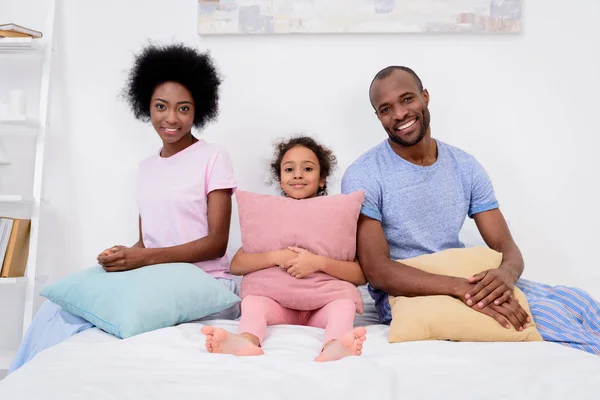 微笑的非洲裔美国人父母和女儿坐在枕头和看相机 — 图库照片