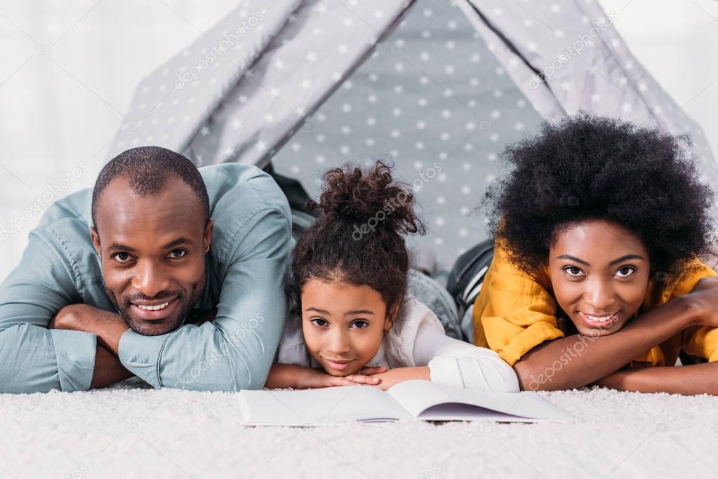 african american parents and daughter lying on floor and looking at camera at home