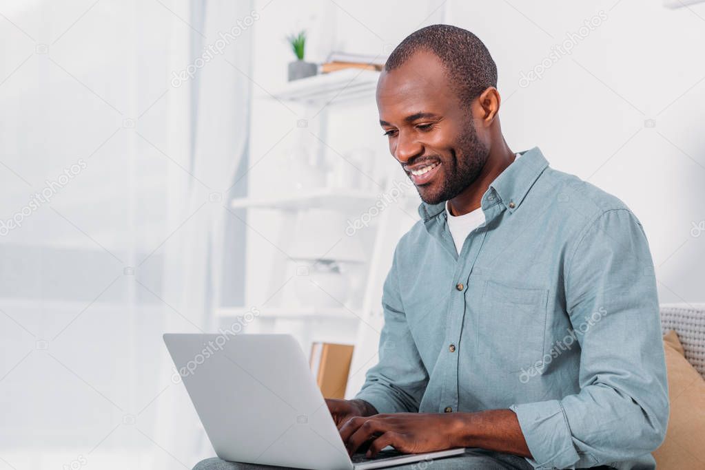 happy african american man using laptop on sofa at home