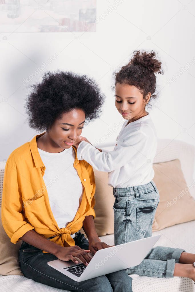 african american mother and daughter looking at laptop at home 