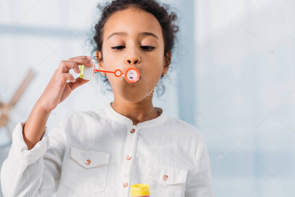 adorable african american kid making soap bubbles at home