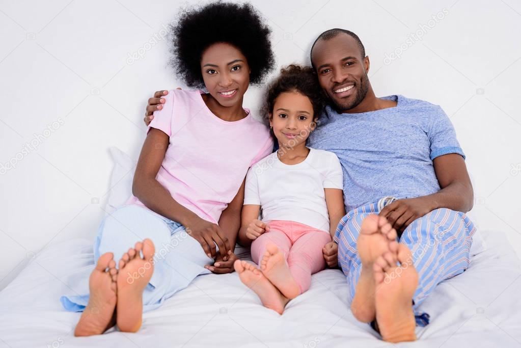 african american parents and daughter lying on bed and looking at camera at home